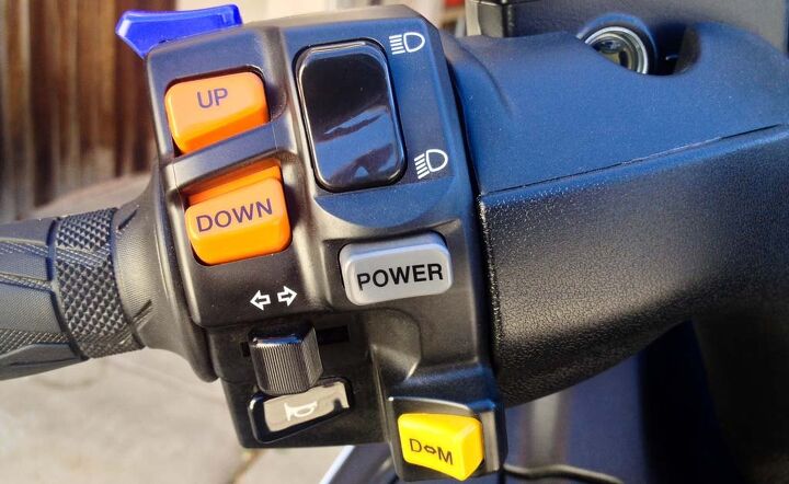 The Burgman’s many options are (from top to bottom): mirror fold switch (blue), thumb shifting (orange), power mode switch (gray), and drive/manual “shift” mode (yellow).